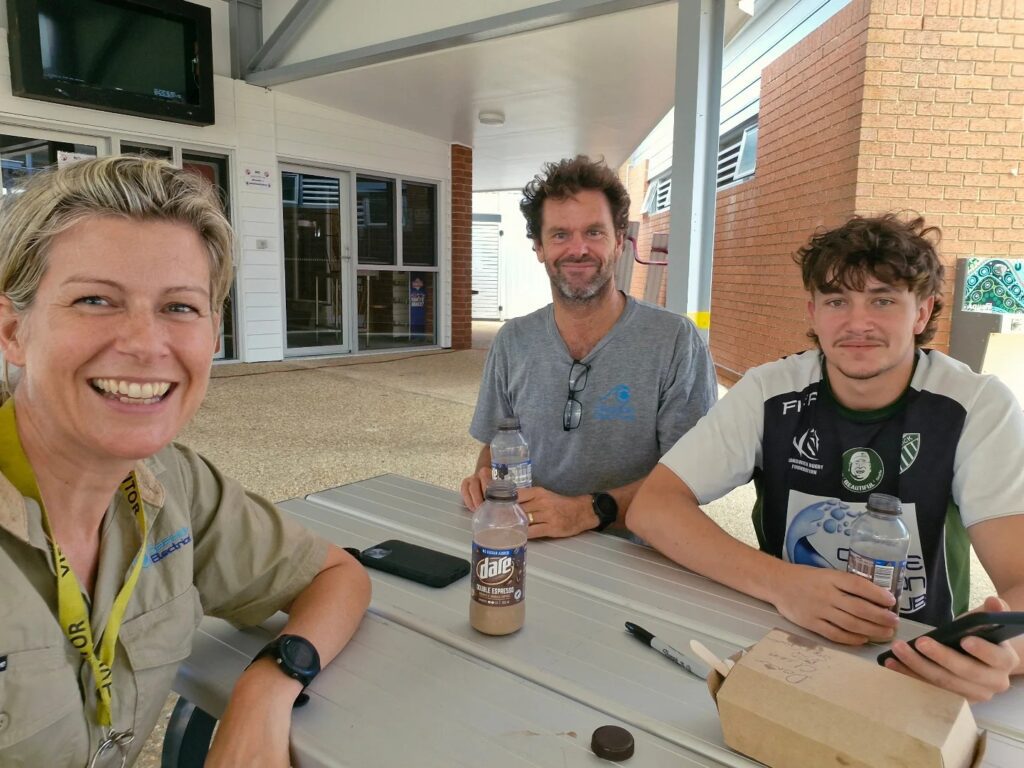 Home Electrician Brad, his wife and his son taking a break from work on a test and tag job, smiling outdoors.